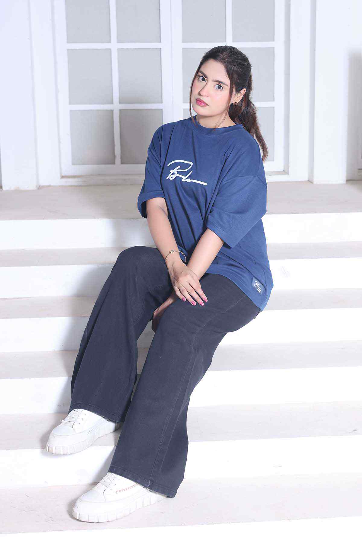 Beleri London blue T-shirt with logo and dark wide-leg pants, seated