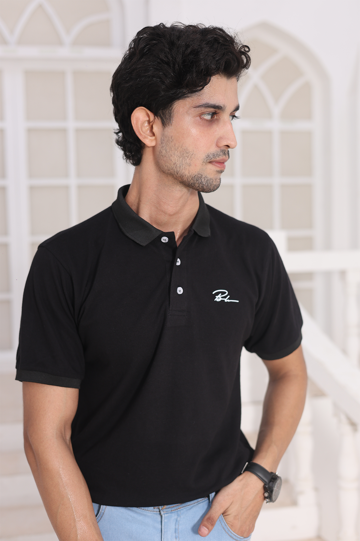 Black polo shirt with buttoned collar and chest logo, model close-up